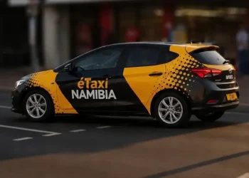 NAMIBIA éTaxi branding: a black and yellow taxi car driving on a city street with dotted pattern on rear side panel.