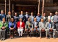 Group of professionals in suits posing for a formal outdoor team photo on a wooden deck.