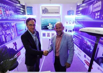 Two businessmen shake hands in a blue-lit trade show booth with Radio Electronic branding and display panels.