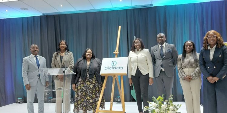 Group of eight professionals in business attire on a stage beside an easel with a DigiNam sign, posing for a photo at a formal event.